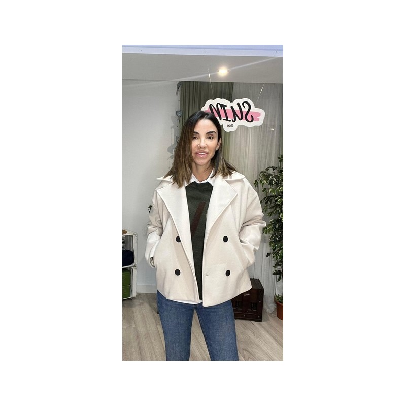 Chaqueta color blanco roto con botones y con solapa y está sin abrochar.